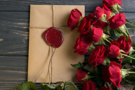 Envelope with wax seal with red rose flowers on wooden tableの写真素材