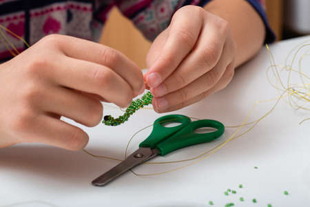 Children hands make bead and wire jewelry on white table