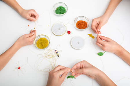 Children hands make bead and wire jewelry on white tableの写真素材