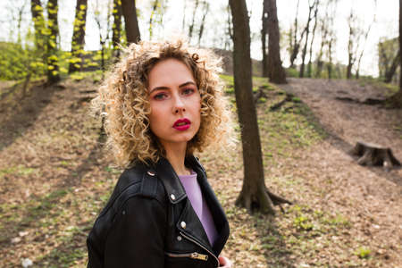 Portrait of a beautiful girl with curly long hair in black leather jacket in the spring forestの写真素材
