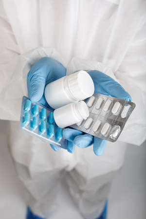 Closeup of doctor's hand in disposable suit and protective gloves holds different pillsの写真素材