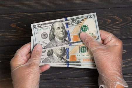 Stack of 100 dollars USA in gloved hands on wooden table