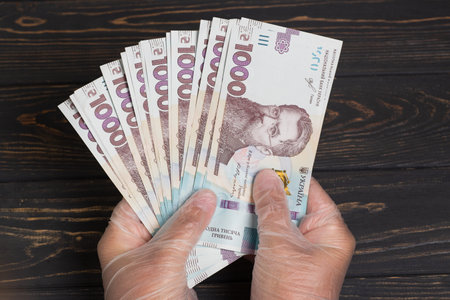 Money of Ukraine. Stack of ukrainian hryvnia banknotes in gloved hands on wooden table. Hryvnia 1000 uahの写真素材