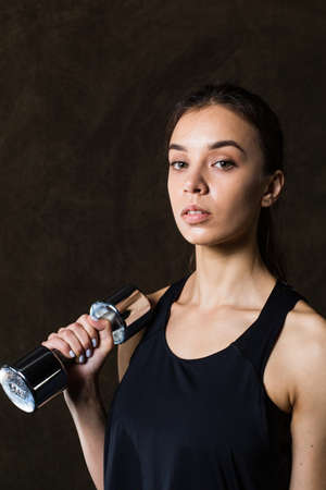 Sporty girl in fashionable sportswear holding dumbbells. Photo of muscular fitness model on dark background. Sports and Healthy lifestyleの写真素材