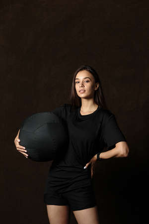 Sporty girl in special sportswear staying with big fitness ball on dark backgroundの写真素材