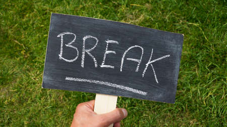Break written on a chalkboard holding in a hand in the parkの写真素材