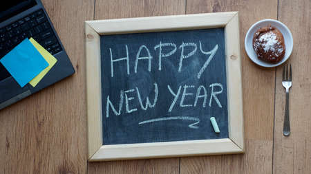 Happy new year written on a chalkboard next to a Dutch donut at the officeの写真素材