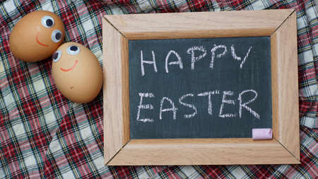 Happy easter wruitten on a chalkboard next to two funny eggsの写真素材