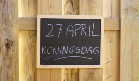 Kingsday in Dutch written on a chalkboard hanging outside at a wooden wallの写真素材