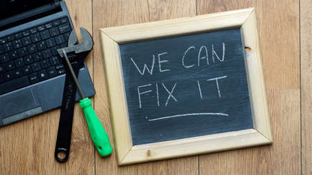 We can fix it written on a chalkboard next to a computerの写真素材