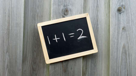 One and one is two written on a chalkboard hanging at a wooden wall