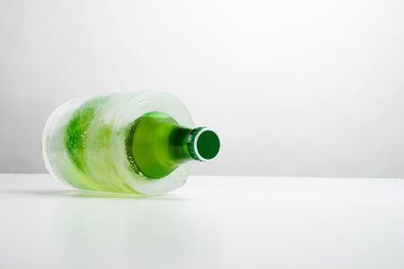 A frozen bottle of beer on white surface.