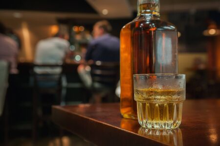 Chilled rocks glass of Bourbon with bottle and people sitting at a bar. の写真素材