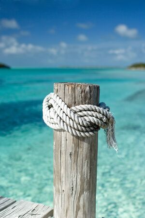 Rope tied to a post on a dock in the ocean.の写真素材