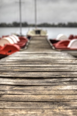 Old wooden dock with paddle boats and sailboat in the background.の写真素材