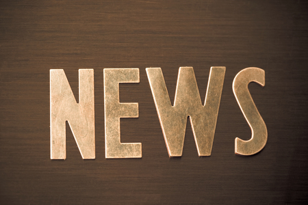 The word NEWS in copper colored letters on wood surface.の写真素材