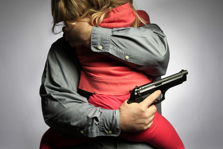 Young child being embraced by a family member with a handgun.
