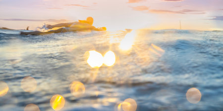 backlit silhouette of a surfer paddling out to surf at sunset