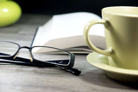 Coffee cup, reading glasses and a bookの写真素材