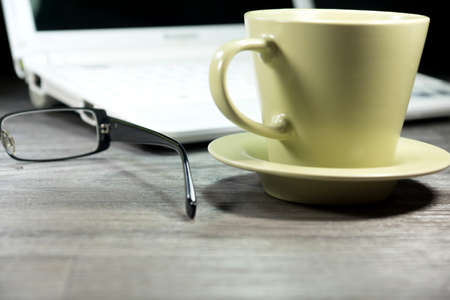 A coffee cup and reading glasses on a office tableの写真素材