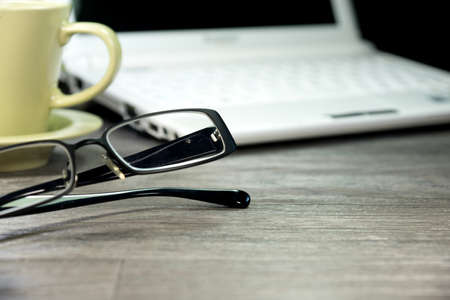 A coffee cup and reading glasses on a office tableの写真素材