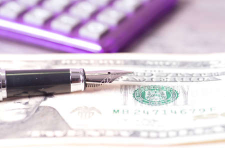 A fountain pen, dollar bills and a pocket calculatorの写真素材