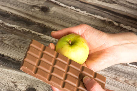 A woman holds an apple and a chocolate in her handsの写真素材