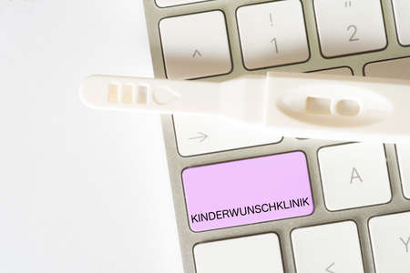 A pregnancy test and a computer keyboard with a button for finding a fertility clinic