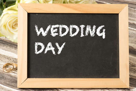 White roses, wedding rings and a chalkboard with the word wedding dayの写真素材