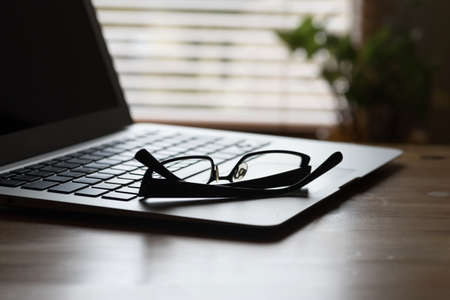 A laptop and reading glasses on a table in the officeの写真素材