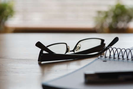 A notebook, reading glasses and a pen on a table in the officeの写真素材