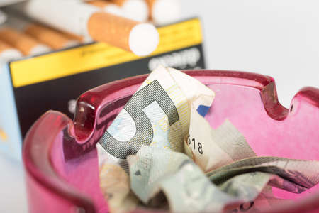 A cigarette and 5 Euro bill in the ashtrayの写真素材