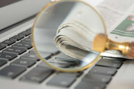 A computer, a newspaper and a magnifying glass