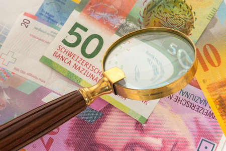 Swiss franc bills and a magnifying glassの写真素材