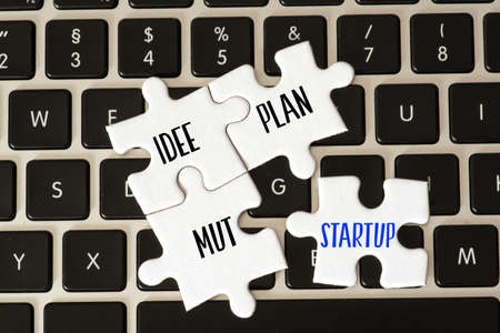 A computer and puzzle pieces with the words startup, idea, plan, courage and goalの写真素材