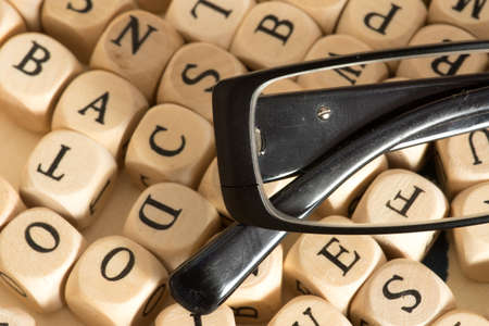 A reading glasses and different wooden letters in the backgroundの写真素材