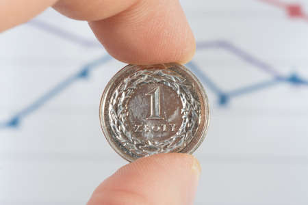 A man holds a coin Polish zloty PLN in front of a diagramの写真素材