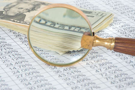 Dollar bills, a magnifying glass and a spreadsheet with numbers and percent