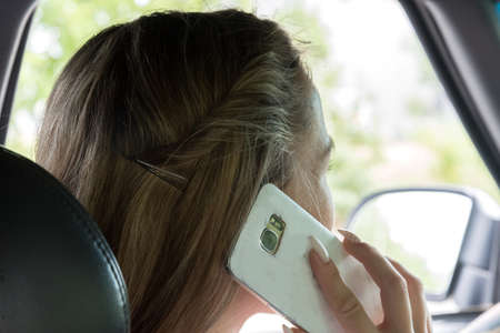 A young woman with mobile phone at the wheelの写真素材