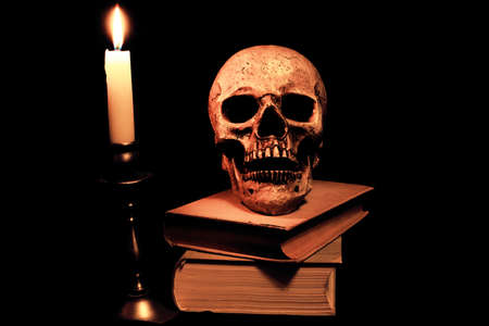 Books and a skull in the light of a candleの写真素材