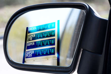 Outside mirror of a car and gas station with expensive fuel