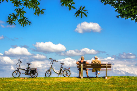 Couple sitting on a bench in the park with bicycles in the backgroundの写真素材