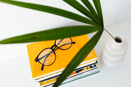 Book and eyeglasses on a white table with a palm leaf