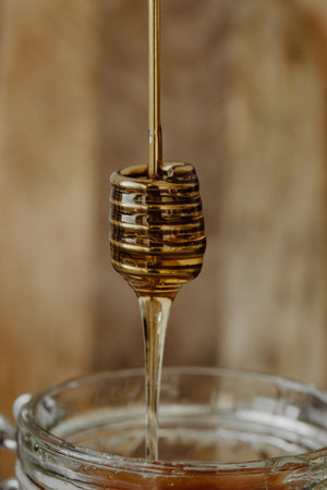 Honey dripping from a wooden honey dipper into a glass jar