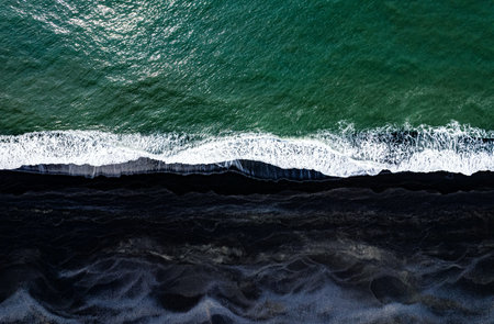 Aerial view of black volcanic sand beach with waves breaking on the shore