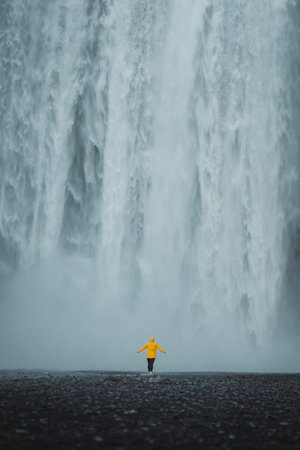 Man in yellow raincoat standing in front of Skogafoss waterfall, Icelandの写真素材