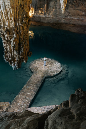 Beautiful bride in a white wedding dress posing in a cave with a stone keyhole on the background of...
