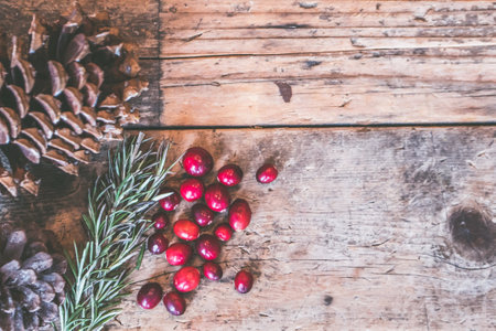 Christmas background with red cranberries, pine cones and rosemary on rustic wooden board
