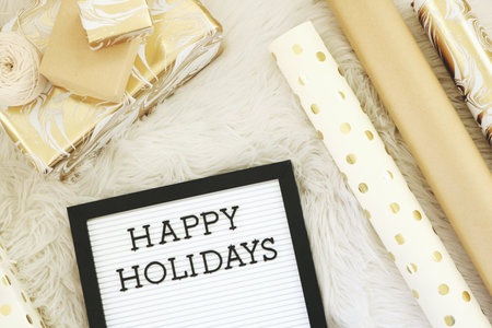 Happy Holidays text on blackboard with gift boxes on white fur background