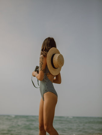 Young woman in swimsuit and hat on the beach with a cameraの写真素材